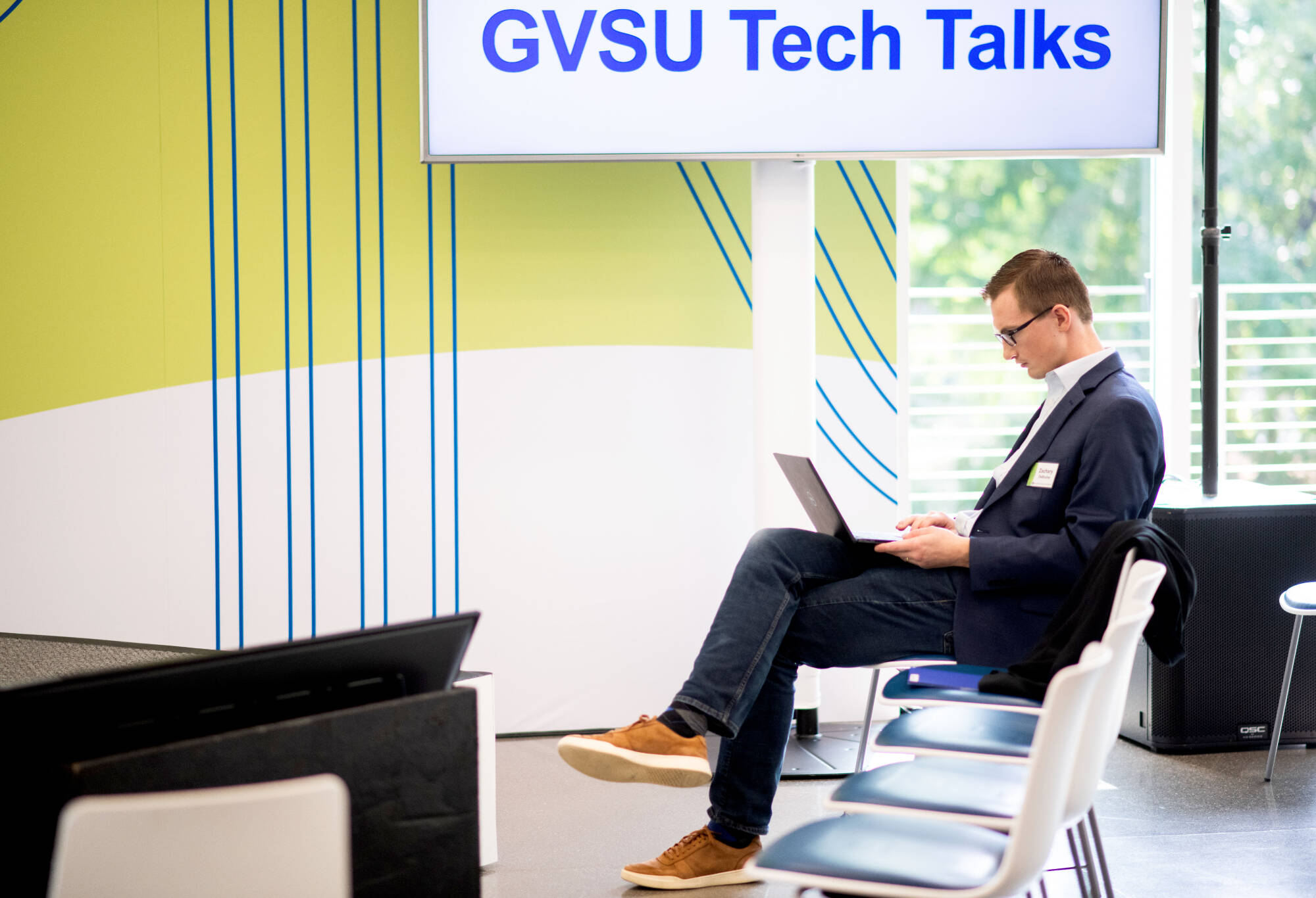 Man seated, using laptop at GVSU Tech Talks event.